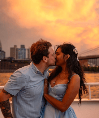 A couple kissing on deck at golden hour, the Manhattan Bridge behind them