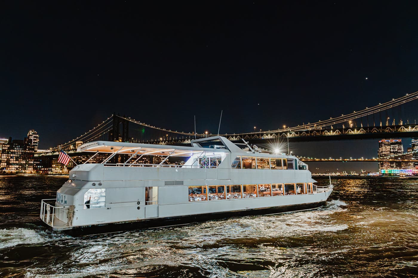 Louisa of the Seas passing beneath the Manhattan Bridge at night, dining saloon lit from within