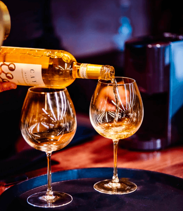 White wine being poured into two glasses at a table